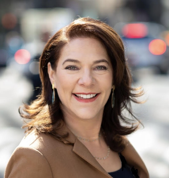 A woman with brown hair and a jacket smiles for the camera.